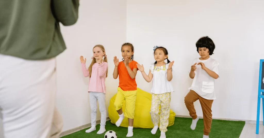 Group of young children following a fitness instructor indoors, practicing balance and coordination exercises