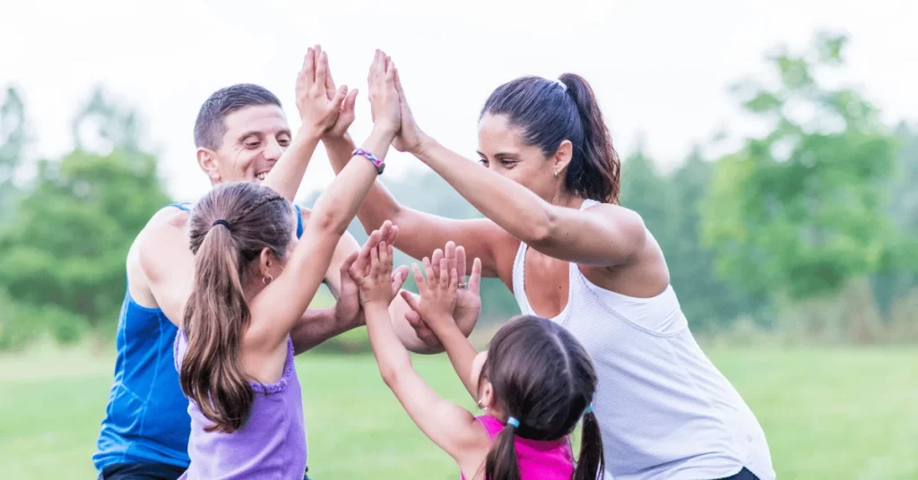 Parents and children celebrating with high fives during an outdoor family fitness activity