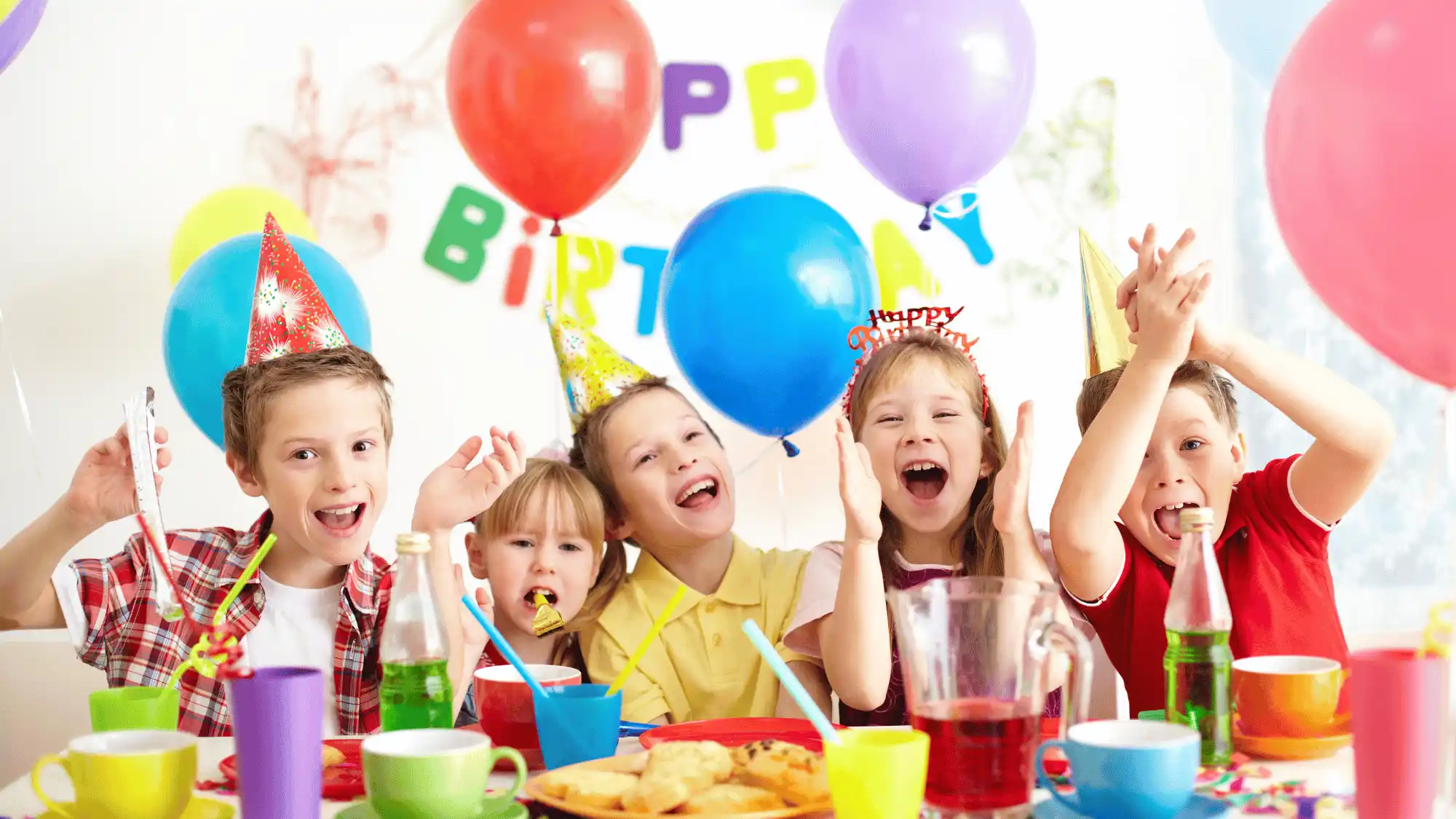 Children celebrating together with balloons, party hats, food, and colorful birthday decorations.