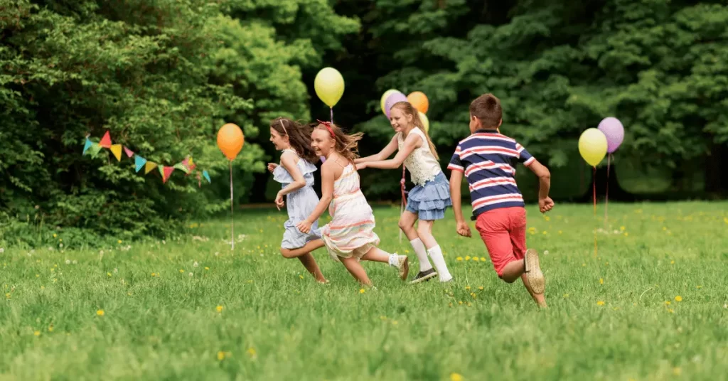 Children running and playing together outdoors during an active birthday party with balloons and decorations.